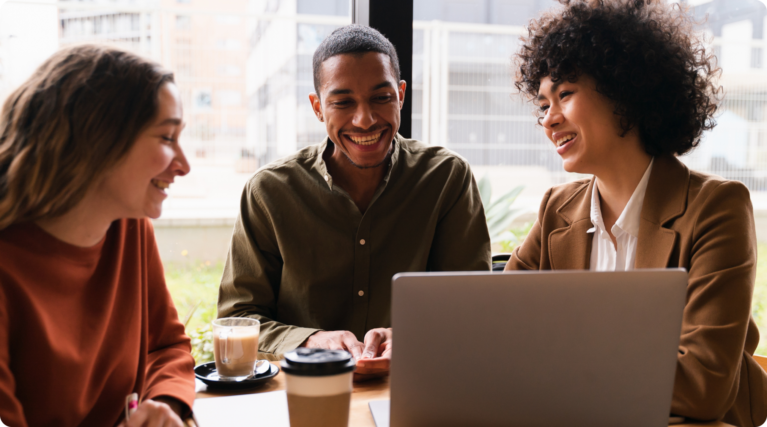Image of two women and one man sitting together at coffee shop table with a laptop